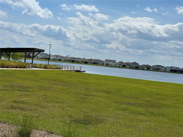 view of dock with a residential view, a water view, and a yard