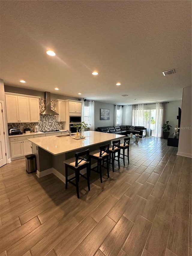 kitchen featuring wall chimney range hood, a large island, white cabinetry, and light countertops