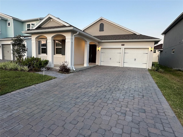 view of front of property with a garage, decorative driveway, a front yard, and stucco siding