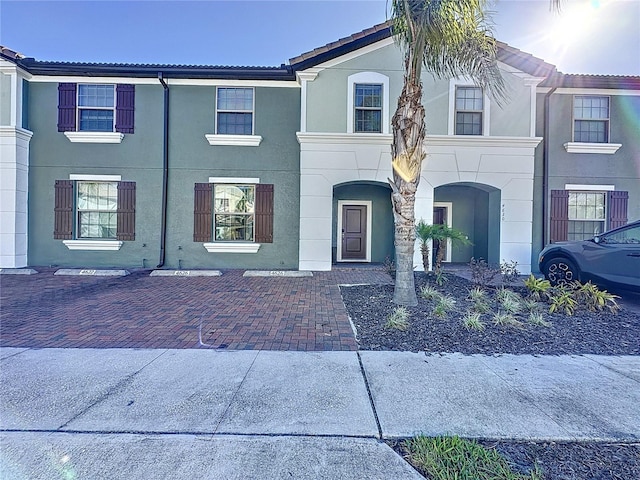 townhome / multi-family property with a tile roof and stucco siding