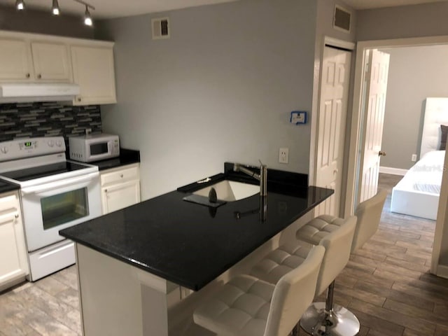 kitchen with a kitchen breakfast bar, backsplash, white appliances, white cabinets, and range hood