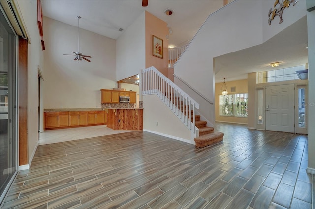 unfurnished living room featuring ceiling fan with notable chandelier and a high ceiling