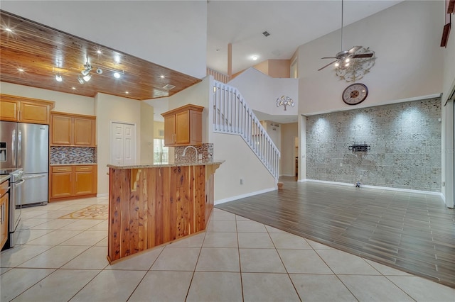 kitchen featuring light stone countertops, appliances with stainless steel finishes, tasteful backsplash, light tile patterned flooring, and kitchen peninsula