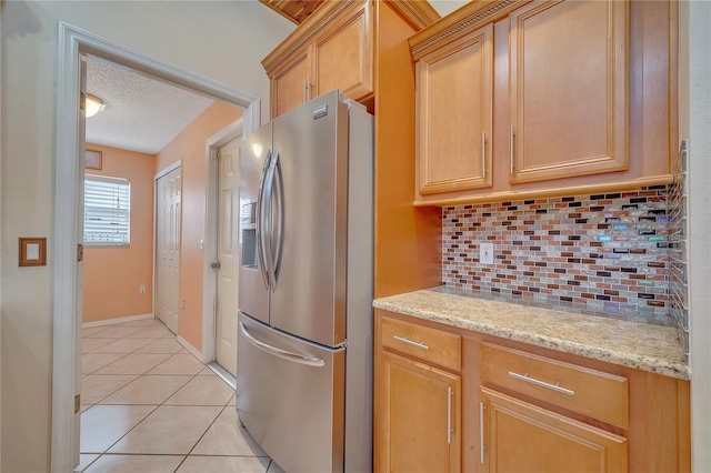 kitchen featuring backsplash, a textured ceiling, light tile patterned flooring, light stone counters, and stainless steel fridge with ice dispenser