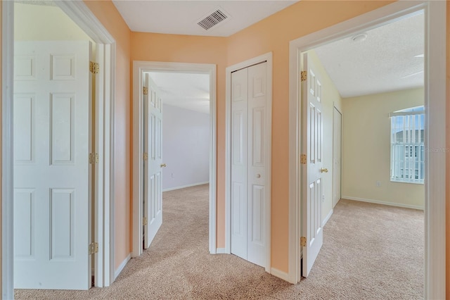 corridor with a textured ceiling and light carpet