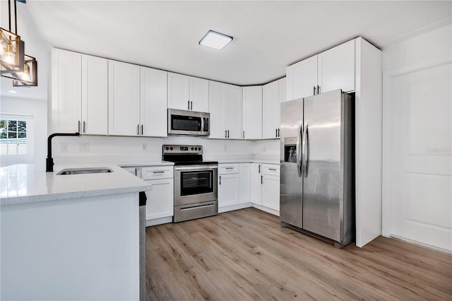 kitchen featuring appliances with stainless steel finishes, light wood-type flooring, sink, pendant lighting, and white cabinetry