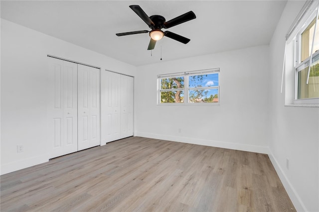 unfurnished bedroom featuring ceiling fan, light hardwood / wood-style flooring, and two closets