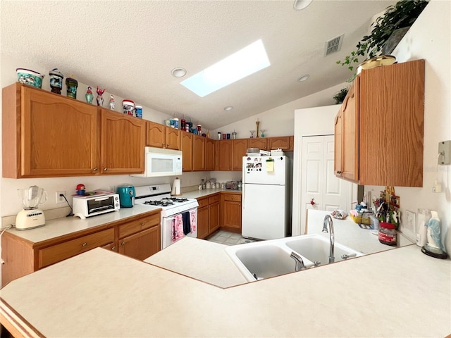 kitchen with kitchen peninsula, white appliances, lofted ceiling with skylight, and sink