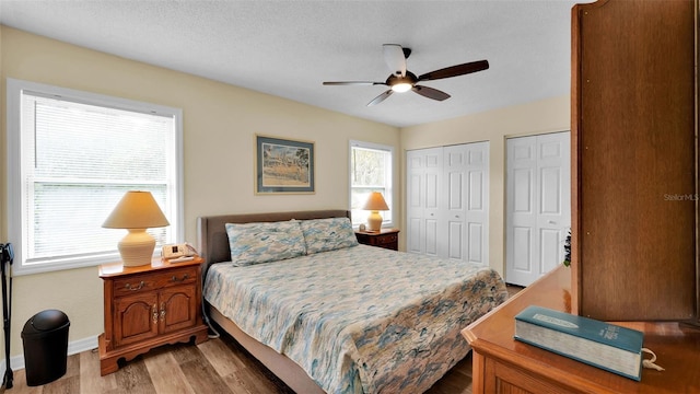 bedroom featuring a textured ceiling, ceiling fan, hardwood / wood-style floors, and two closets