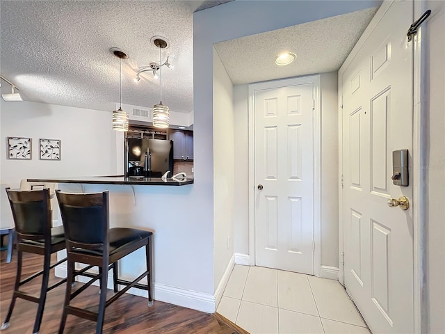 kitchen with stainless steel fridge with ice dispenser, tile patterned flooring, kitchen peninsula, decorative light fixtures, and a kitchen bar