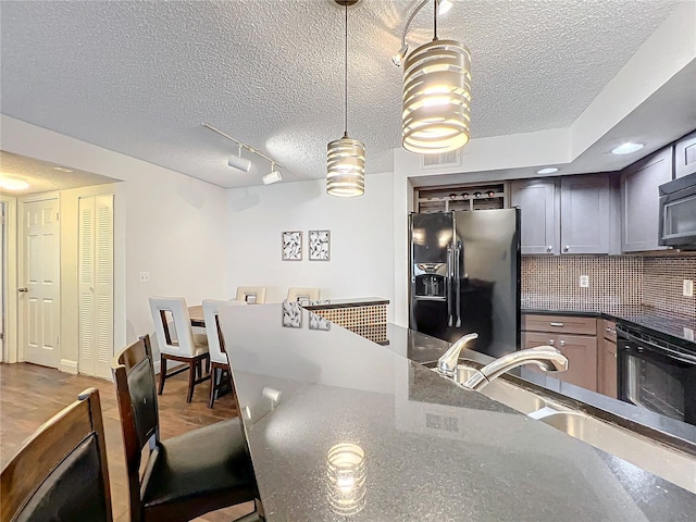 kitchen with hanging light fixtures, dark stone countertops, stainless steel fridge, a textured ceiling, and decorative backsplash