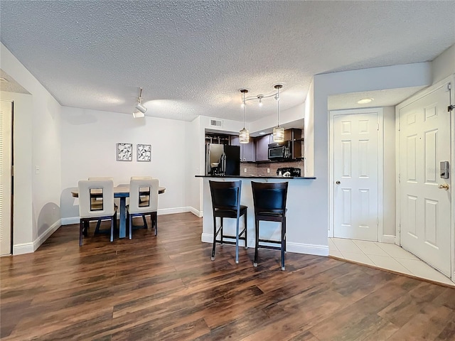 kitchen featuring a kitchen breakfast bar, stainless steel fridge, dark brown cabinets, dark hardwood / wood-style flooring, and kitchen peninsula