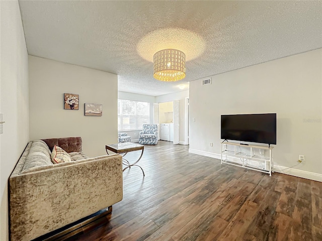 living room featuring a textured ceiling, hardwood / wood-style flooring, a notable chandelier, and washing machine and clothes dryer