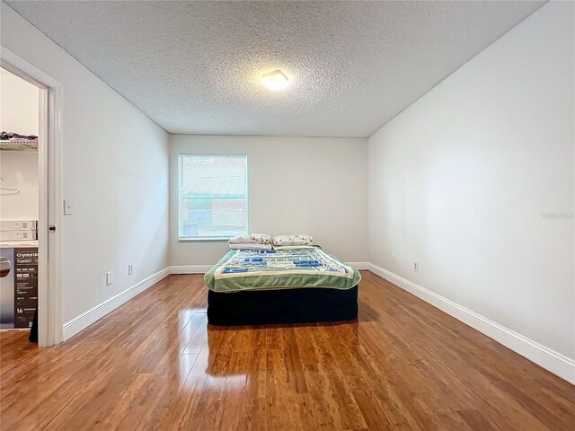 bedroom with hardwood / wood-style floors, a walk in closet, and a textured ceiling