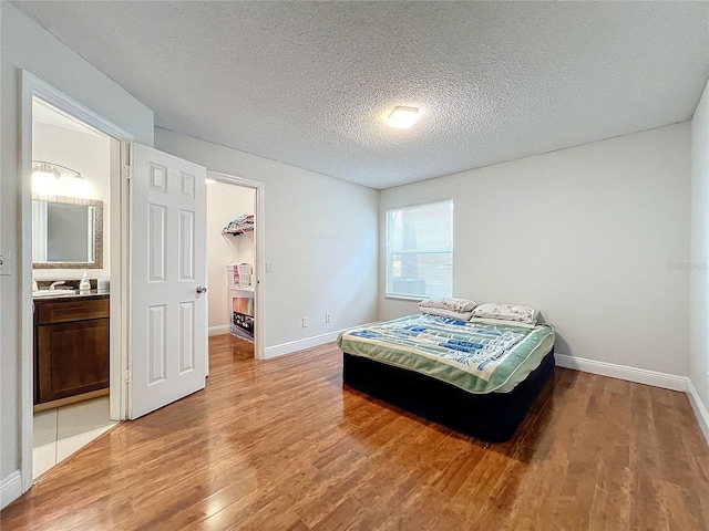 bedroom featuring a walk in closet, ensuite bathroom, a textured ceiling, hardwood / wood-style floors, and a closet