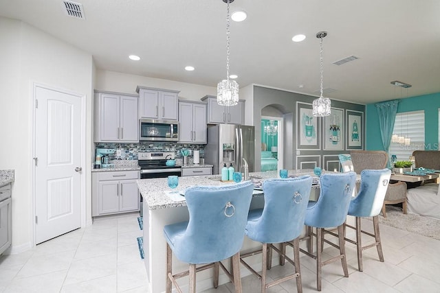 kitchen featuring a center island with sink, decorative light fixtures, gray cabinets, and appliances with stainless steel finishes