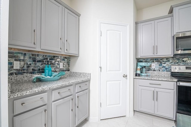 kitchen with decorative backsplash, stainless steel appliances, light stone countertops, and light tile patterned flooring