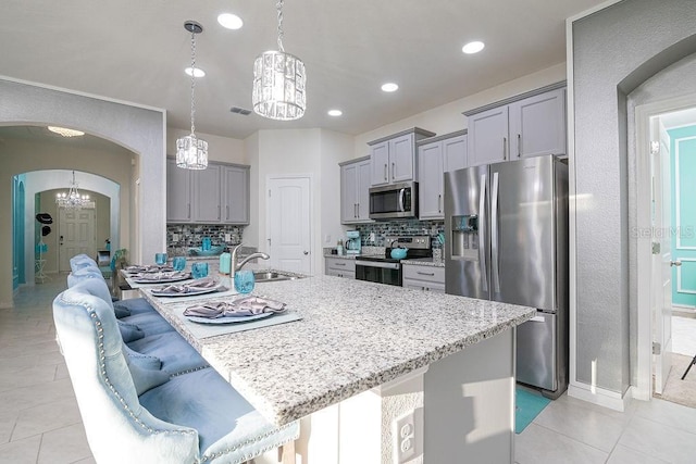 kitchen with a kitchen bar, stainless steel appliances, sink, hanging light fixtures, and an island with sink