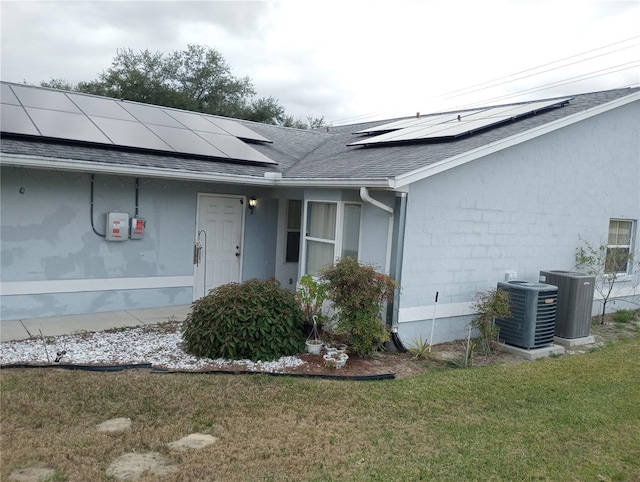 entrance to property featuring central air condition unit, a lawn, and solar panels