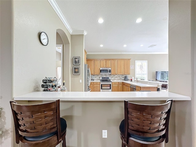 kitchen featuring kitchen peninsula, appliances with stainless steel finishes, tasteful backsplash, ornamental molding, and a breakfast bar