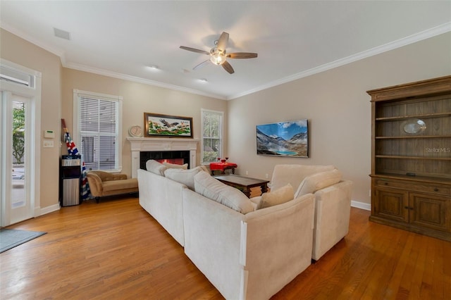 living room with ceiling fan, crown molding, wood-type flooring, plenty of natural light, and a tiled fireplace