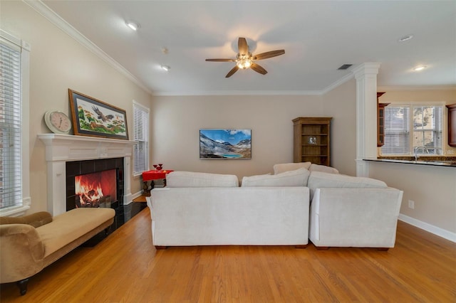 living room featuring hardwood / wood-style flooring, ceiling fan, crown molding, and a tiled fireplace