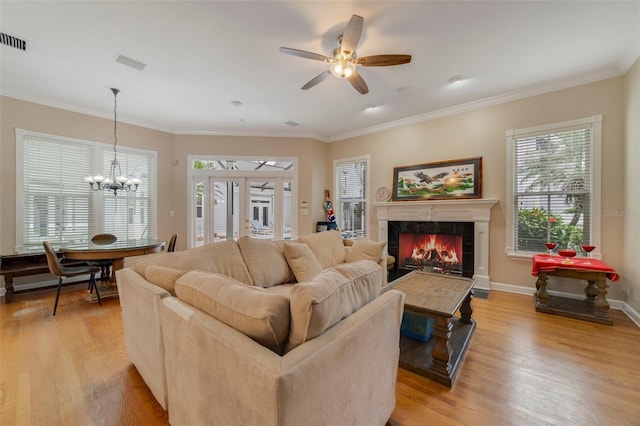 living room with a tile fireplace, crown molding, ceiling fan with notable chandelier, and light wood-type flooring