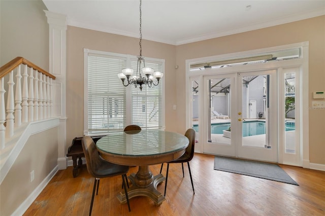 dining area with ornamental molding, french doors, wood-type flooring, and an inviting chandelier