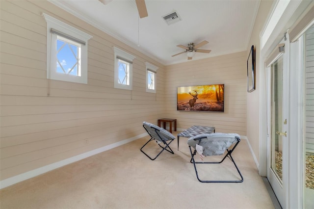 living area featuring light colored carpet, ceiling fan, crown molding, and wood walls