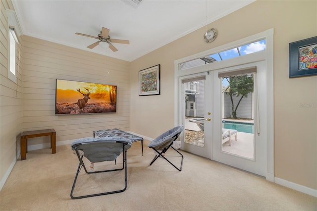 living area featuring french doors, light colored carpet, ceiling fan, wooden walls, and crown molding