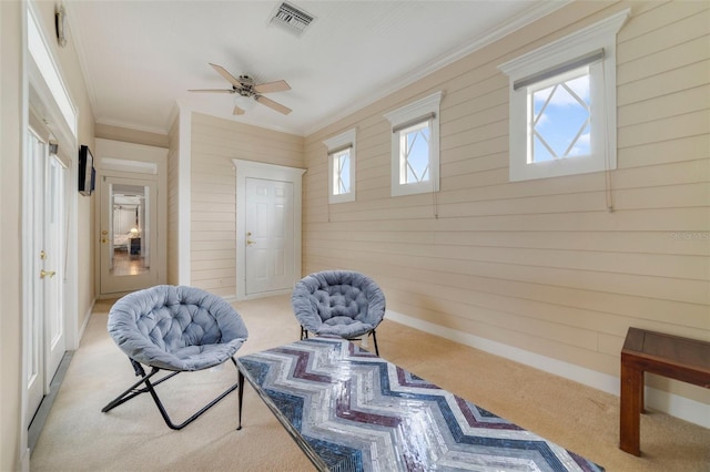 sitting room with light carpet, plenty of natural light, wooden walls, and ceiling fan