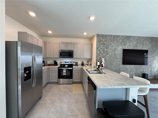 kitchen featuring sink, kitchen peninsula, a breakfast bar area, gray cabinets, and appliances with stainless steel finishes