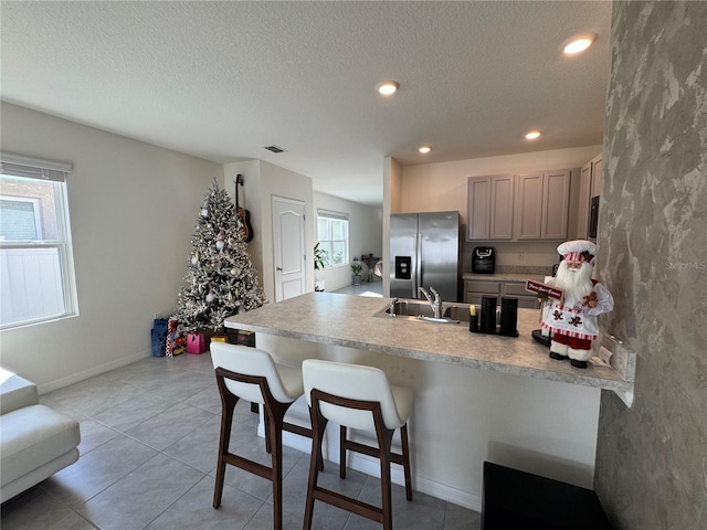 kitchen with sink, kitchen peninsula, stainless steel fridge, gray cabinets, and a breakfast bar