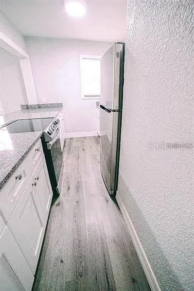 kitchen with light stone counters, white cabinetry, stainless steel appliances, and light hardwood / wood-style flooring