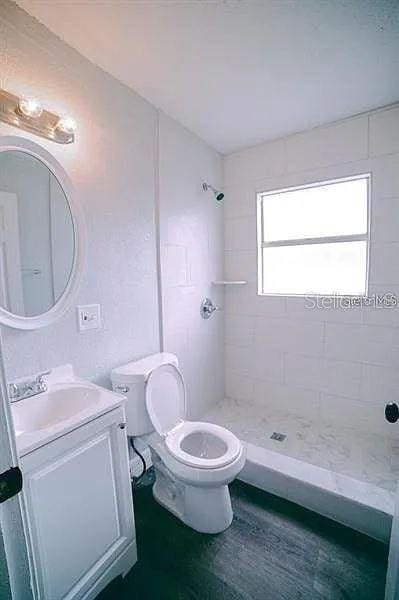 bathroom with a tile shower, vanity, wood-type flooring, and toilet