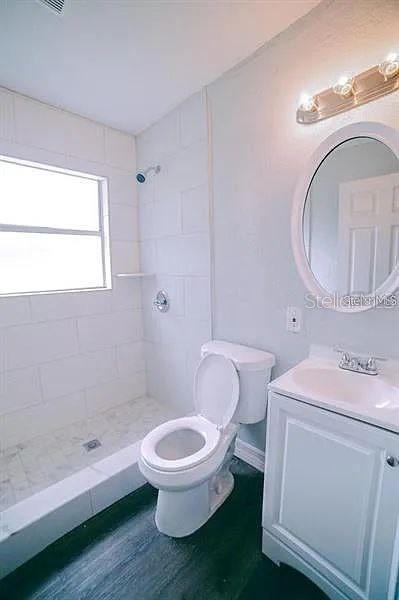 bathroom with a tile shower, vanity, toilet, and wood-type flooring