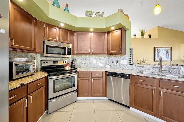 kitchen featuring light stone countertops, sink, stainless steel appliances, decorative light fixtures, and light tile patterned floors