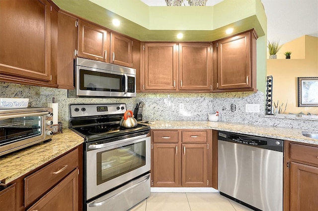 kitchen featuring backsplash, light stone counters, light tile patterned floors, and appliances with stainless steel finishes