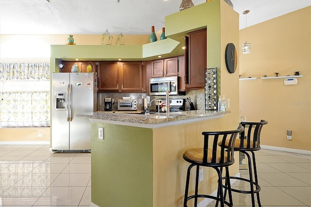 kitchen with decorative backsplash, a kitchen breakfast bar, kitchen peninsula, stainless steel appliances, and light tile patterned flooring