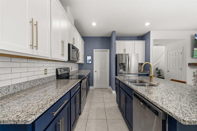 kitchen with stainless steel appliances, blue cabinets, sink, a center island with sink, and white cabinets