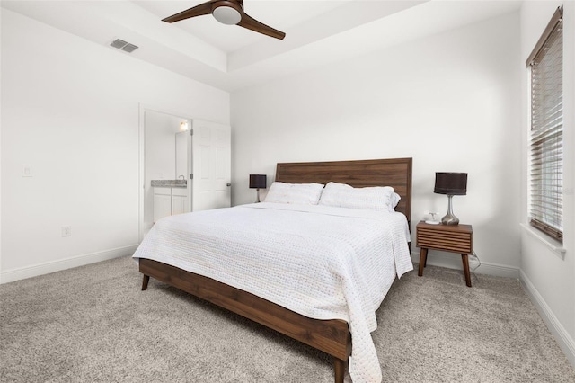 bedroom with light carpet, a tray ceiling, ensuite bath, and ceiling fan