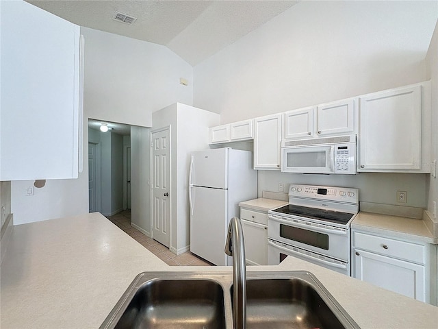 kitchen with white appliances, vaulted ceiling, sink, light tile patterned floors, and white cabinets