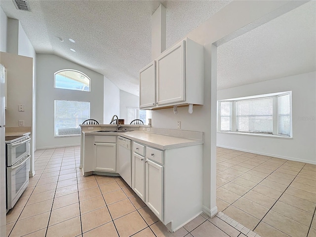 kitchen with kitchen peninsula, stove, light tile patterned floors, white cabinets, and lofted ceiling