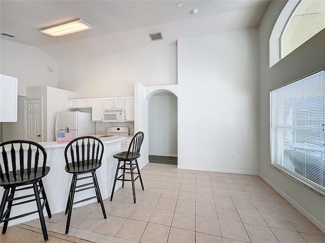 kitchen with white appliances, white cabinets, a textured ceiling, light tile patterned flooring, and a kitchen bar