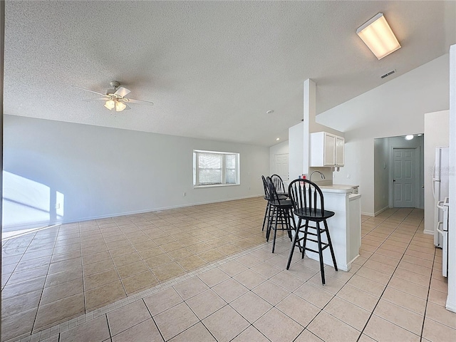 kitchen with white cabinetry, kitchen peninsula, vaulted ceiling, a kitchen bar, and light tile patterned floors