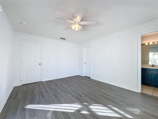 unfurnished bedroom with dark wood-type flooring, ensuite bathroom, sink, ceiling fan, and a textured ceiling