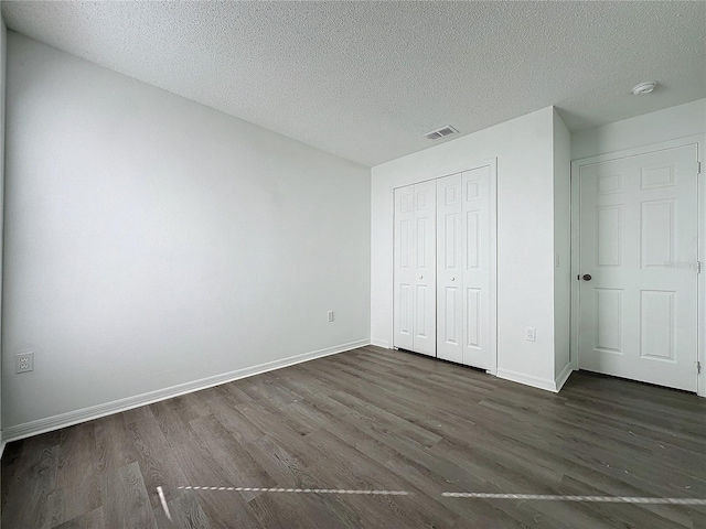 unfurnished bedroom with a textured ceiling, a closet, and dark wood-type flooring