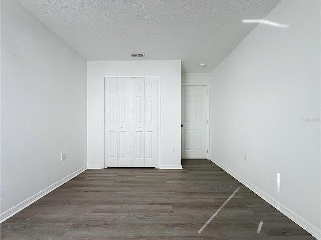 unfurnished bedroom with dark hardwood / wood-style floors, a textured ceiling, and a closet