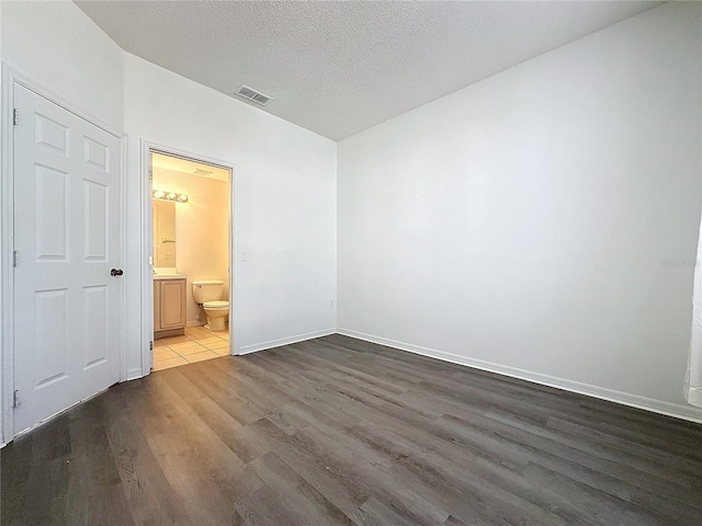 unfurnished bedroom with a textured ceiling, dark wood-type flooring, and ensuite bath