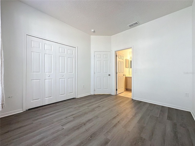 unfurnished bedroom with ensuite bath, a closet, a textured ceiling, and hardwood / wood-style flooring